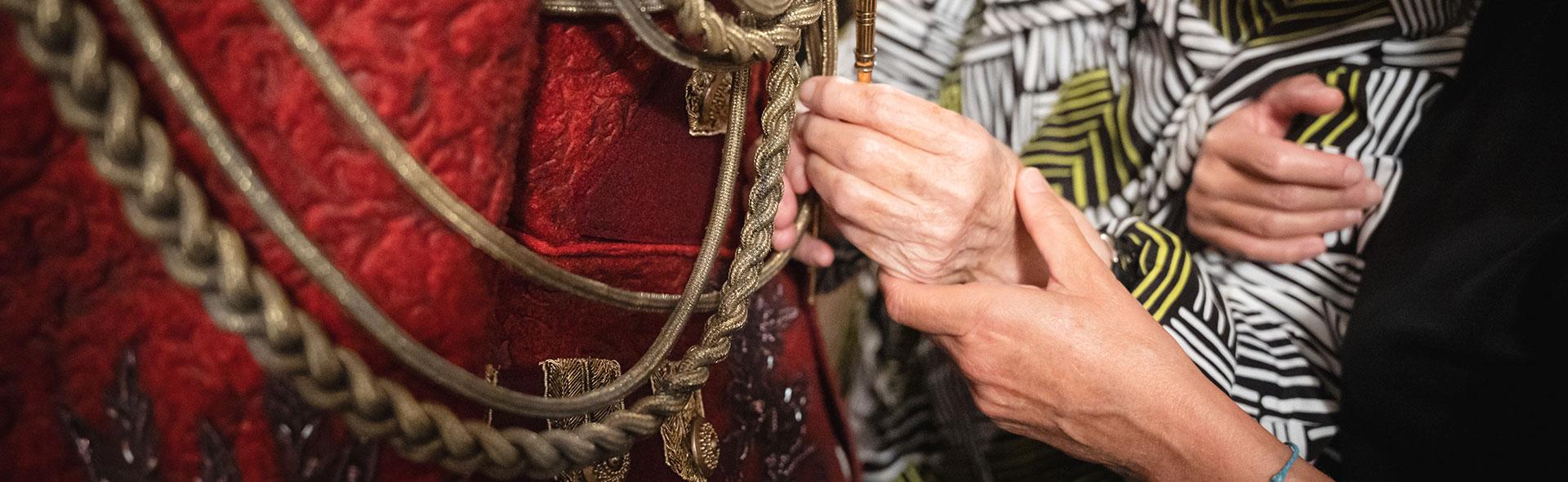 © Marta Cervone Dettaglio di due mani che toccano un costume dello spettacolo “Il barone rampante” di Italo Calvino, diretto dal regista Riccardo Frati. Il costume è un’uniforme militare di colore rosso, in stile settecentesco, con cordelline dorate.